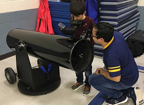Father and son look through Dobsonian telescope